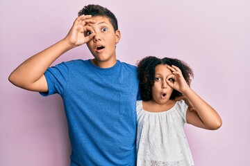 Young hispanic family of brother and sister wearing casual clothes together doing ok gesture shocked with surprised face, eye looking through fingers. unbelieving expression.