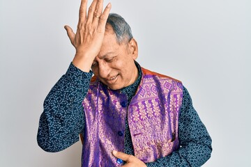 Middle age indian man wearing traditional indian clothes surprised with hand on head for mistake,...