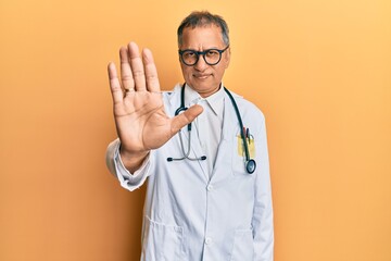 Middle age indian man wearing doctor coat and stethoscope doing stop sing with palm of the hand....