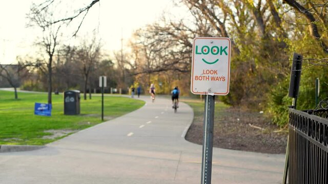 Cyclist and joggers pass a sign that reads look both ways on the White Rock Lake bike and jogging path in Dallas Texas