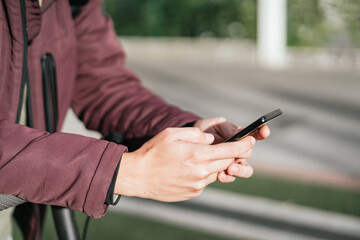 Hands of a person sending a message with his cell phone on the electric scooter.
