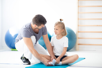 Obraz premium Cute school girl sitting on blue yoga mat talking to her handsome young physician