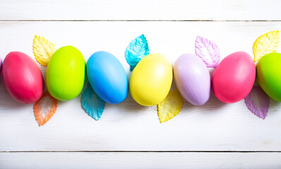 Bright Easter eggs with colored leaves are laid out in a row on a white wooden background. Easter background.