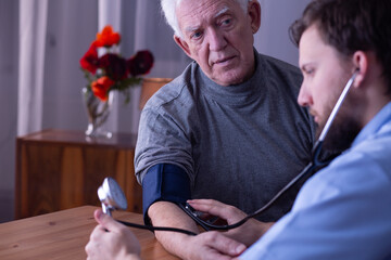 Young male nurse measuring blood pressure of senior man