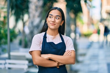 Young latin barista girl with arms crossed smiling happy at the coffee shop