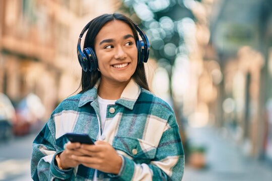 Young latin girl smiling happy using smartphone and headphones at the city.
