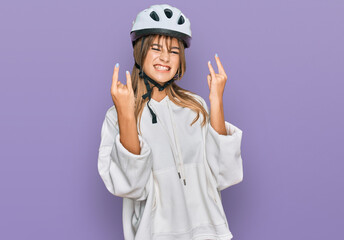 Teenager caucasian girl wearing bike helmet shouting with crazy expression doing rock symbol with hands up. music star. heavy concept.
