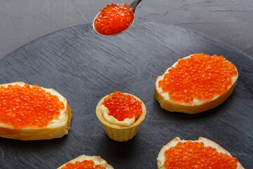 Fototapeta na wymiar Bruschetta with butter and red caviar on a black board in a row.
