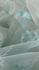 airy organza with emerald embroidery is rolled up with light waves of fabric, transparent material for tulle or curtains with green floral embroidered print lies in careless folds