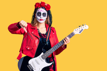 Obraz na płótnie Canvas Woman wearing day of the dead costume playing electric guitar with angry face, negative sign showing dislike with thumbs down, rejection concept