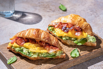 croissant sandwich breakfast with scrambled egg, crispy bacon and mashed avocado