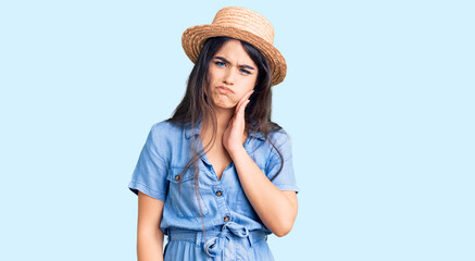Brunette teenager girl wearing summer hat touching mouth with hand with painful expression because...