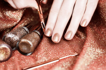 Woman making manicure by herself. Female hands with bronze-colored manicure on a shiny bronze background.