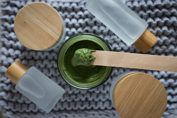 Horizontal view of facial homemade cosmetic clay on a bamboo stick surrounded by some tonic cosmetic bottles.