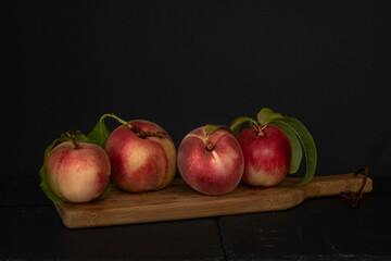 Fresh peaches  with leaves against black background on a wooden board: four whol , with leaves, viewed form an angle
