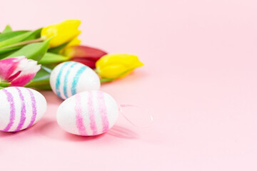 Easter painted eggs with tulips on a pink background. Copy space. Easter celebration concept.