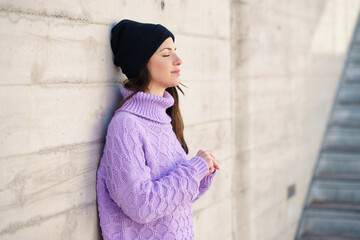 Woman in her twenties leaning against a wall outside with her eyes closed.