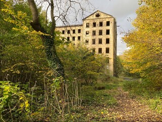 Obraz premium Derelict old stone mill, with wild plants, and trees, on a cloudy day on, Lee Bank, Halifax, UK