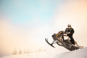 Fotobehang The rider in gear with a helmet making snow jumping on a snowmobile on a background of a winter scenic landscape with mounting and sky. © igor tsarev 