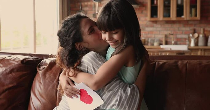 Loving 10s daughter congratulates mommy with Mother day, prepare postcard with drawn red heart. Happy mommy kiss hug cute child express gratitude for received post card. Life event celebration concept
