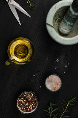 Layout of products for cooking seasoning in a marble mortar. Composition with sea salt, rosemary, olive oil and various types of pepper on a dark wooden background, top view