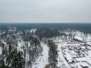 Obraz premium Snow-covered houses in a pine forest. Aerial drone view. Winter snowy morning.