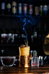 Alcoholic cocktail with orange on wooden. yellow cocktail with a smoking garnish with copy space. Vertical photo of a yellow cocktail with a Cortez