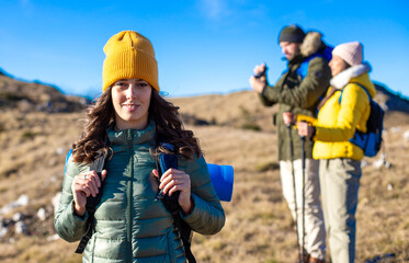 Portrait of a smiling woman hiking at the top of the mountain. A group of friends is enjoying the fresh air and sun.	