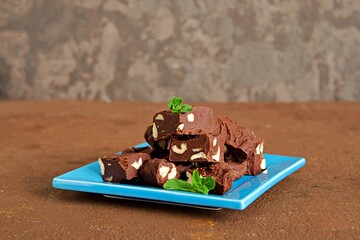 Sliced homemade fudge chocolates made from dark chocolate, condensed milk and hazelnuts on a blue plate on a brown concrete background. Candy recipes. American cuisine.