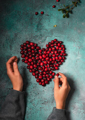 Child's hands making a heart shape with cranberry mors berries. Healthy vegan food concept. Rustic background. Still life. © Oksana Schmidt