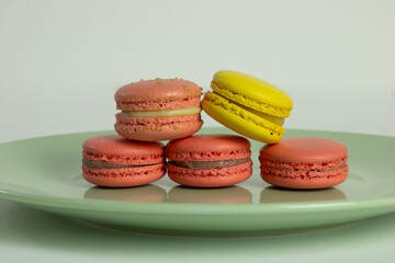 Yellow and pink Macaroons in a green plate with a white background