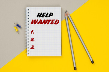 On a yellow-gray background are pencils, buttons and a notebook in which it is written - HELP WANTED
