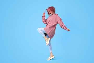 Tattooed girl in jeans, hoodie and sneakers with colored curly pink hair dancing and having fun