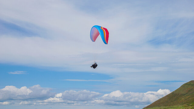 Paragliding above the clouds over Rhossili bay of Gower peninsula in the UK, beautiful blue sky and green field background