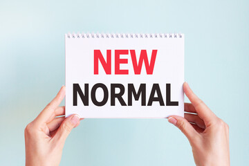 NEW NORMAL word inscription on white card paper sheet in hands of a woman. Business concept