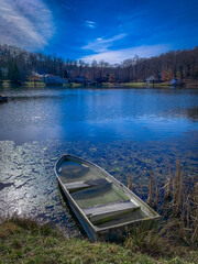 Portrait of a Half-Flooded Boat at the Edge of a Residential Pond on a Bright, Sunny Day with Blue Skies