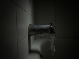 Dark, Moody Side View of a Running Bathtub Faucet, with Water Pouring Out into the Tub