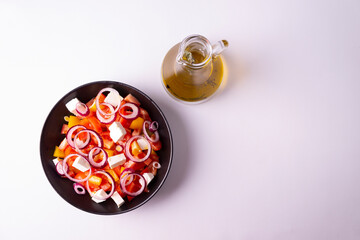 Greek salad in a black plate and a bottle of olive oil on a white background. Horizontal orientation. Flat lay.