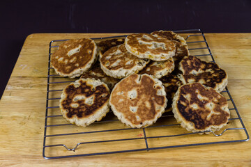 Freshly cooked sugared welshcakes on a cooling rack on wooden board.