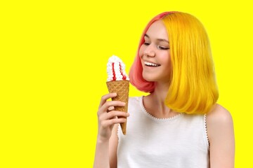 Smiling model teenager with ice cream in waffle cone over yellow background