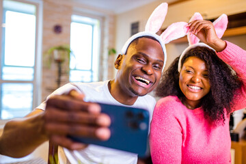 Young african american man and woman wearing cute easter bunny ears in the house taking selfie on...