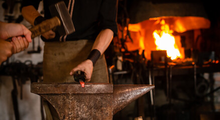 blacksmith with striker forges a horseshoe on the anvil with forging chisel, close-up blacksmith...