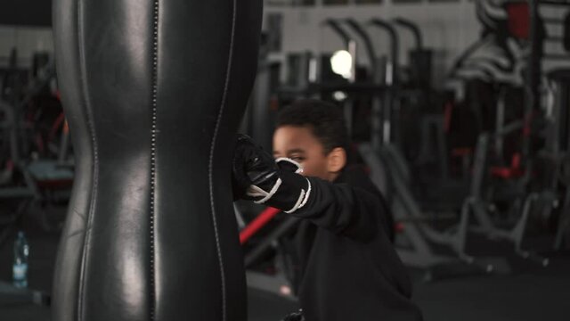 A school-aged boy is boxing at dark gym. African american.