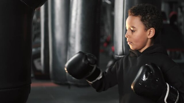 A school-aged boy is boxing at dark gym. African american.