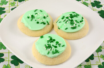 St Patrick's Day cookies with green icing and sprinkles on white plate on shamrock tablecloth
