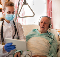 Nurse helping senior man in hospital to make conference call with family