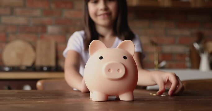 Little adorable kid girl sit alone in kitchen putting insert coins into piggy bank, close up view. Younger gen and saving pocket money, invest think for future, manage personal savings economy concept