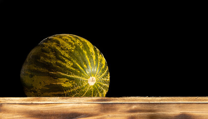 Green melon, for sale at farmers market, black background, on wood.