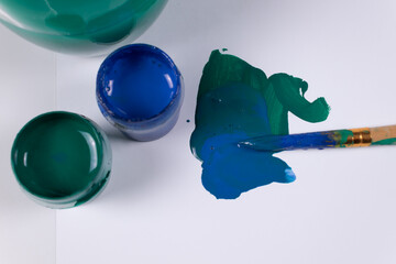 top view of two jars of blue and green gouache, a couple of green and blue strokes and a stained brush on them, top view