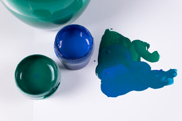 two strokes and two jars of green and blue gouache, against the background of a jar of water for brushes